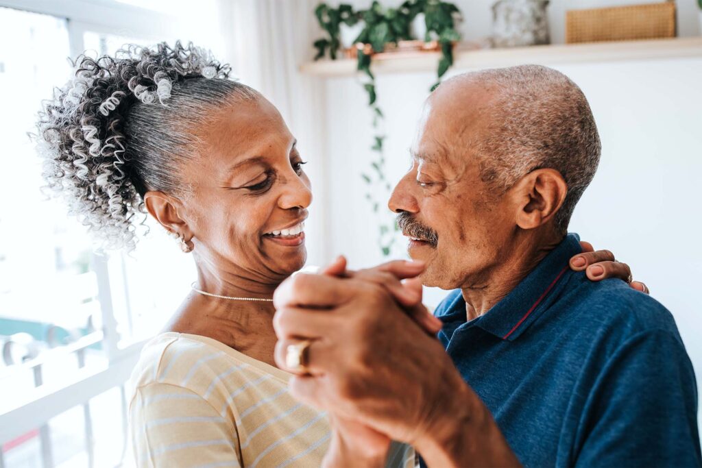 Mature couple smiling and dancing in their home.